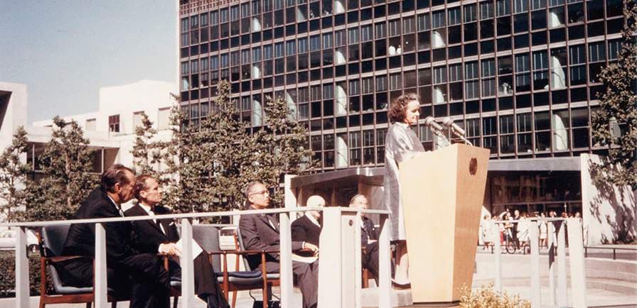 Barbara Hepworth speaking at a podium with men in suits sitting behind her