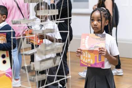 A child holding a colourful leaflet looking at a sculpture