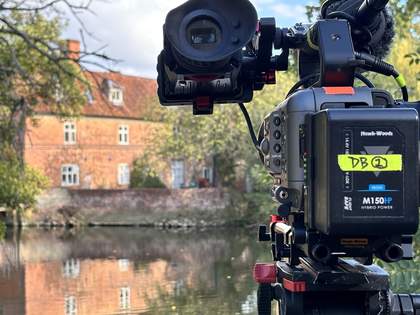 A film camera set up in front of a cottage and a lake